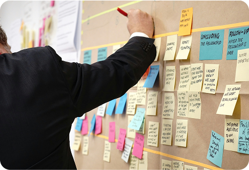 Business professional in suit pointing at colorful sticky notes on wall during project planning session