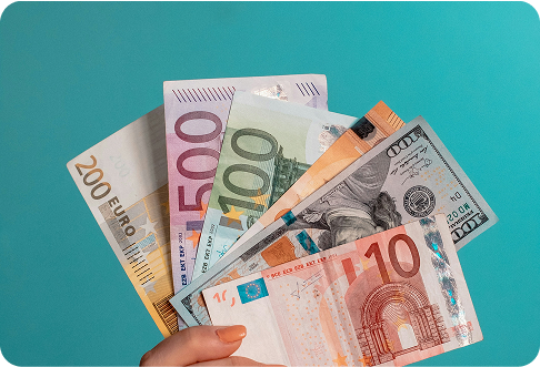 Person holding mixed euro and dollar banknotes including 10, 100, 500 euro bills and US dollars on teal background