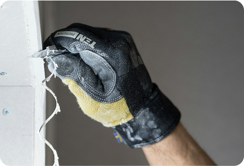 Person wearing black work glove sanding drywall corner with sandpaper during home renovation