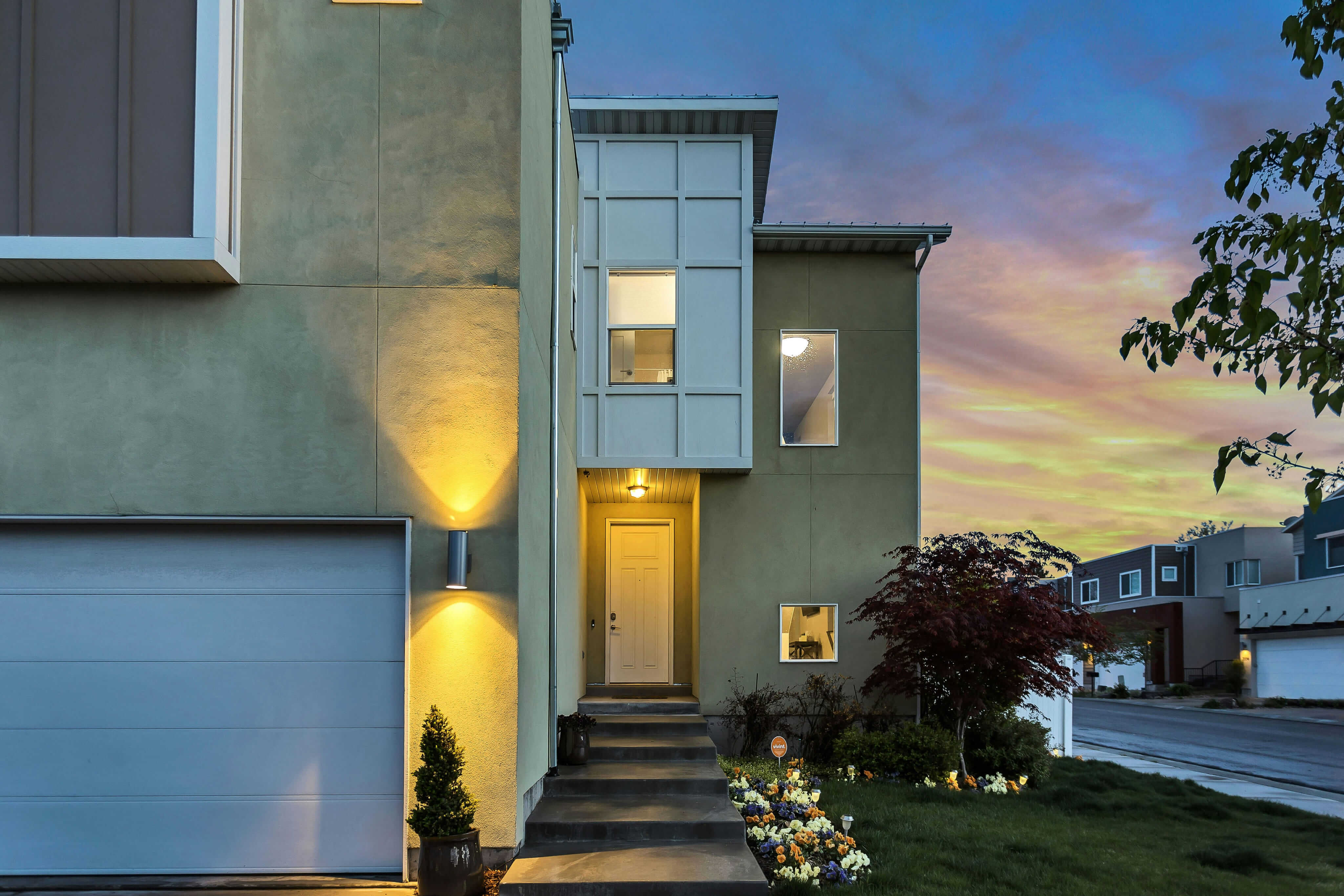 Modern suburban home with attached garage, illuminated entryway, and landscaped front yard at sunset